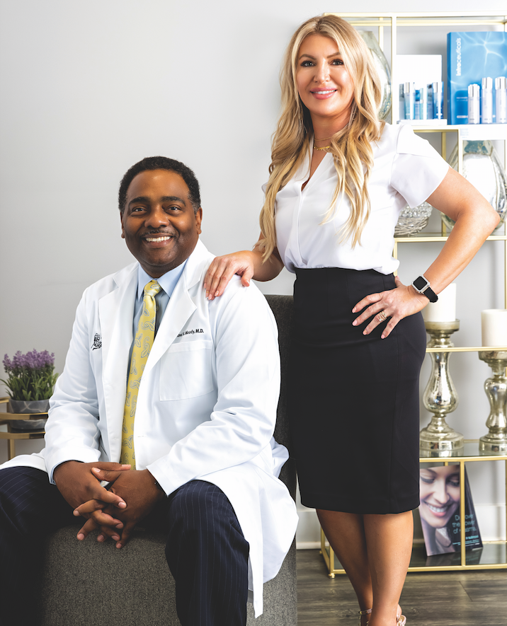 Dr. Michael Moody and Melissa Romero in front of a beige wall and gold and glass shelf